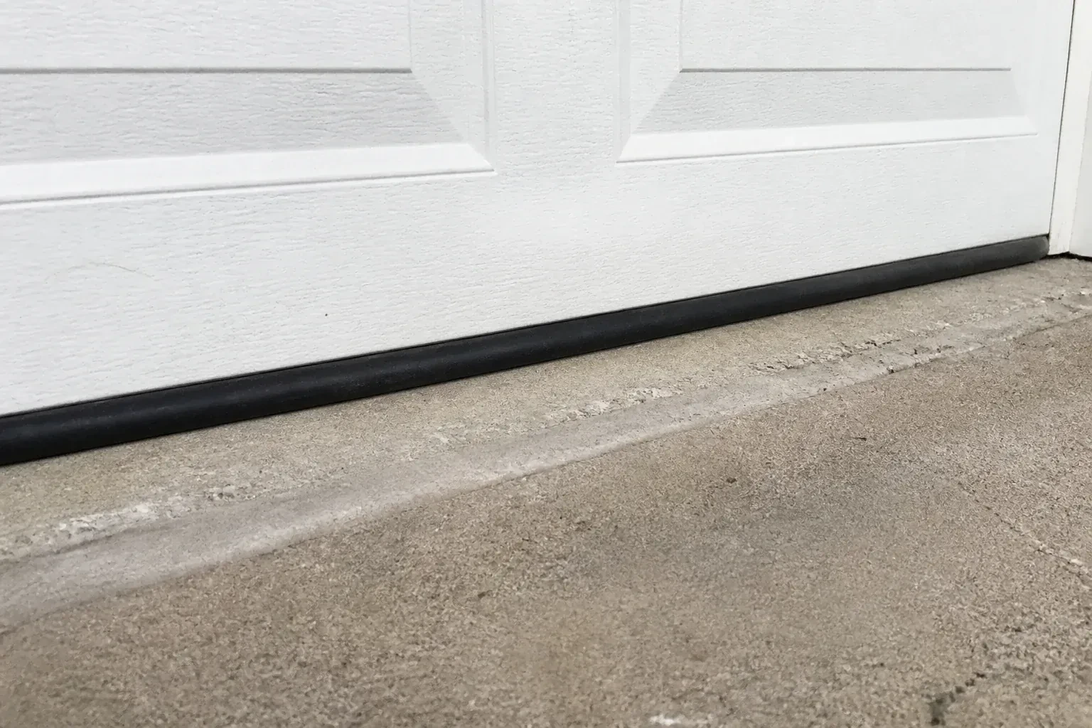 Black bottom seal along a closed white garage door at a concrete threshold. — Garage Door Bottom Seal Replacement, Lincoln