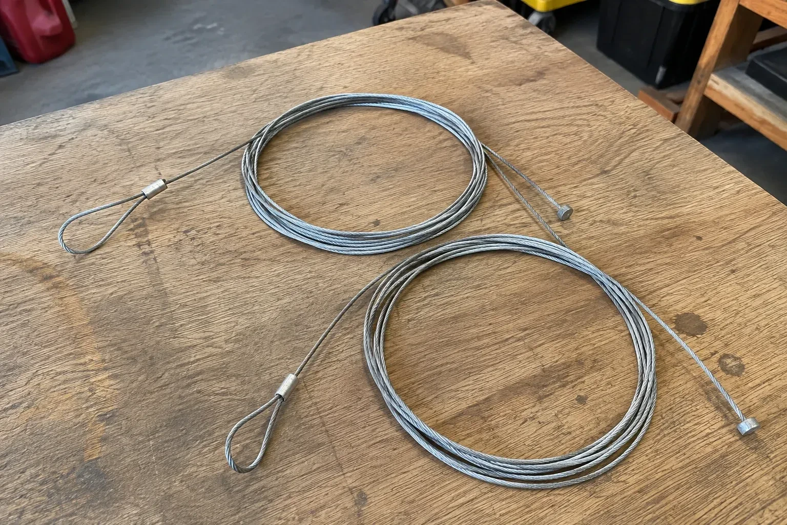 Two coiled steel cables with loop and stop ends on a workbench. — Garage Door Cable Replacement, Lincoln