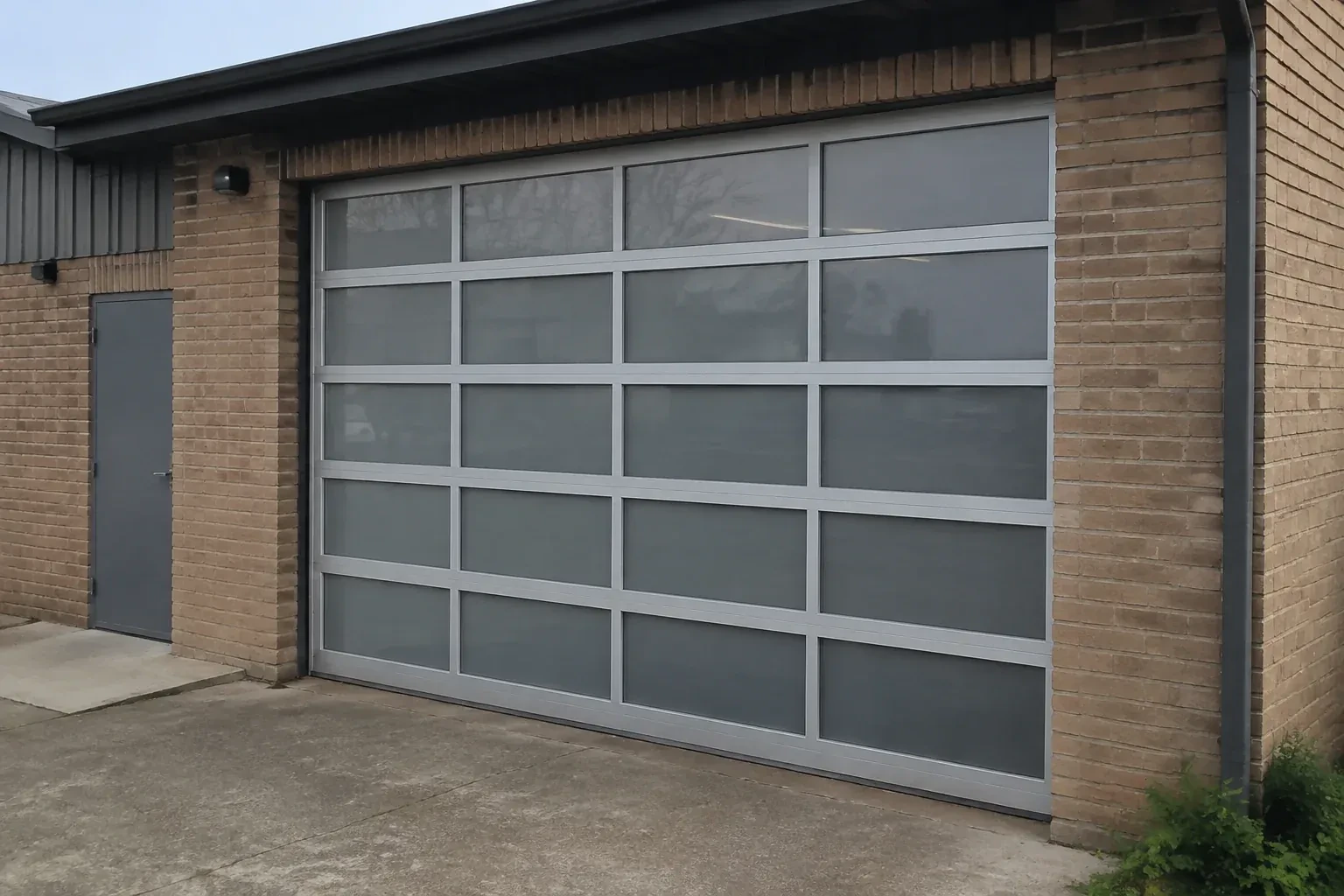 Closed glazed sectional door in a grey metal frame at a brick workshop. — Full-View Glass Garage Door Installation, Lincoln